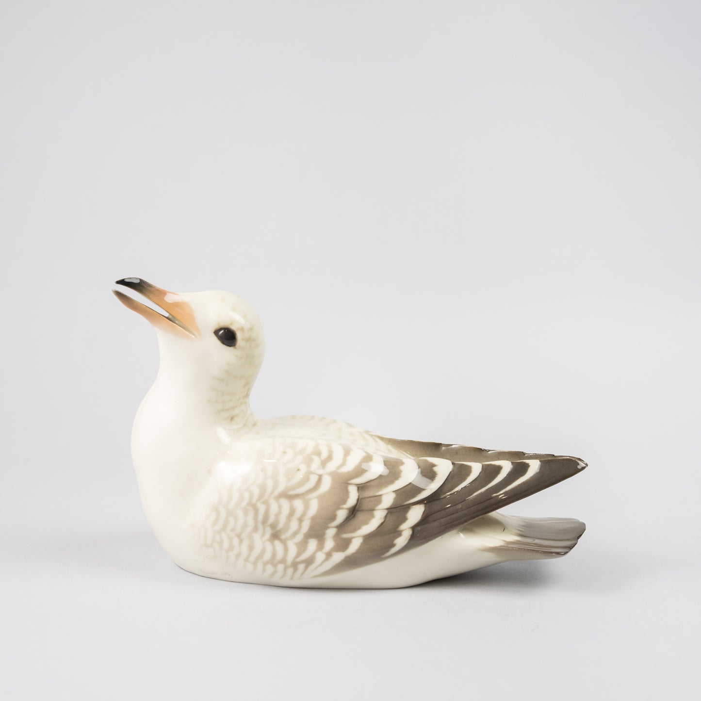 Mås i underglasyrteknik, 1920-tal. Tillverkad på Rörstrand och såld hos Löfbergs i Malmö. 11,5cm hög och 19cm lång. Gull in porcelain painted with underglazed technic, 1920's. Made by Rörstrand. H: 11,5cm/4,5" and W: 19cm/7,5".